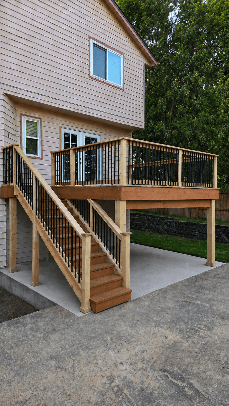 Elevated wooden deck with black metal railings and stairs leading down to a concrete patio.