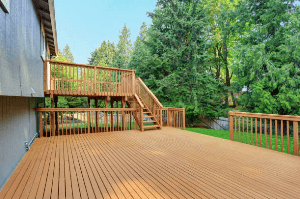 Spacious tiered wooden deck with stairs attached to a house, surrounded by lush green trees.