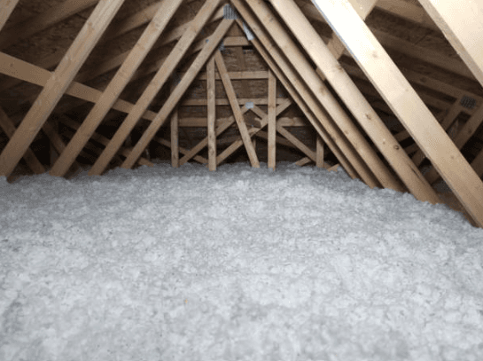 White blown-in insulation covers the floor of an attic space framed with wooden roof trusses.