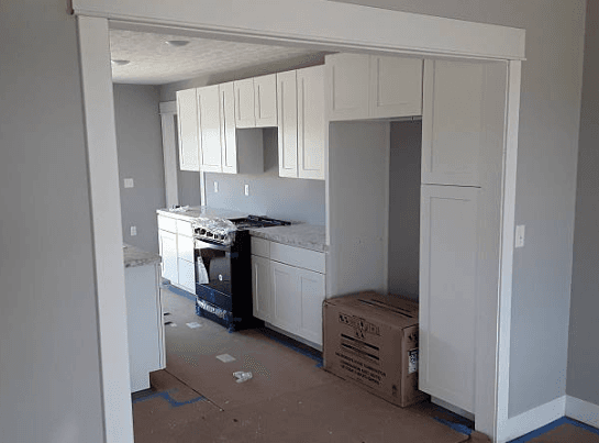 Modern kitchen under construction with white shaker cabinets, a black stove, and gray walls.